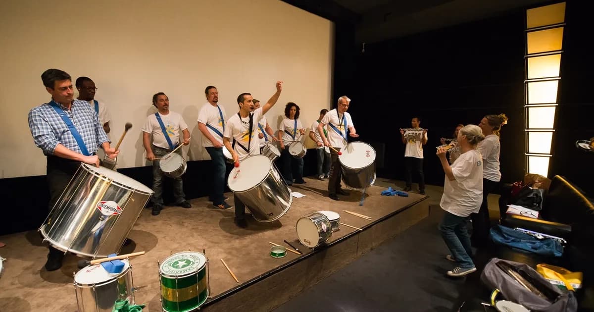 Atelier batucada sur scène : des participants aux surdos suivent le bras levé qui donne le signal au groupe, Pessoa Connect