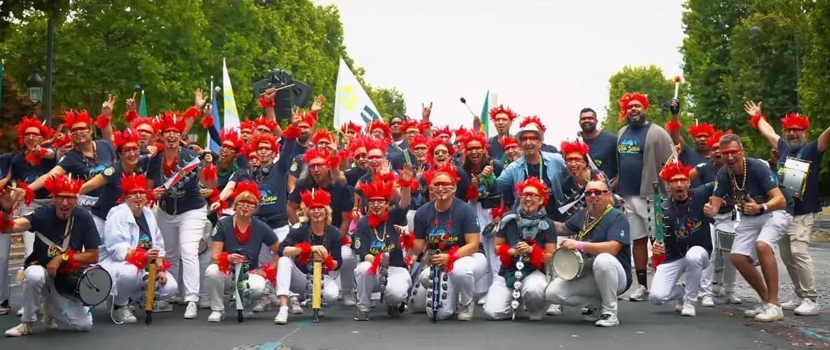 Bateria de l'école de samba Vila Sena réunie en extérieur, percussionnistes en coiffes rouges, instruments en main
